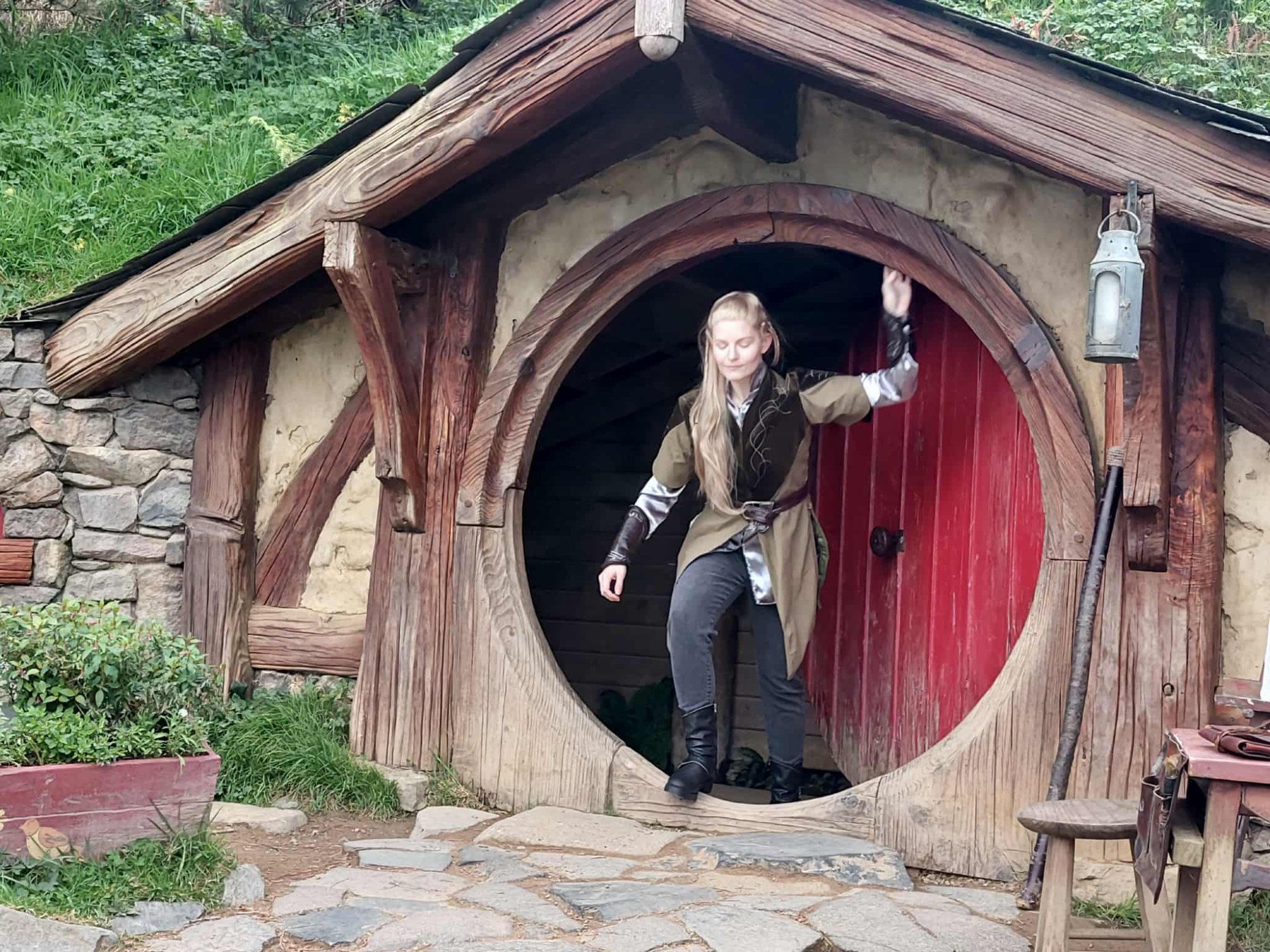 Visitor stepping out of a hobbit hole with iconic round red door at Hobbiton Movie Set