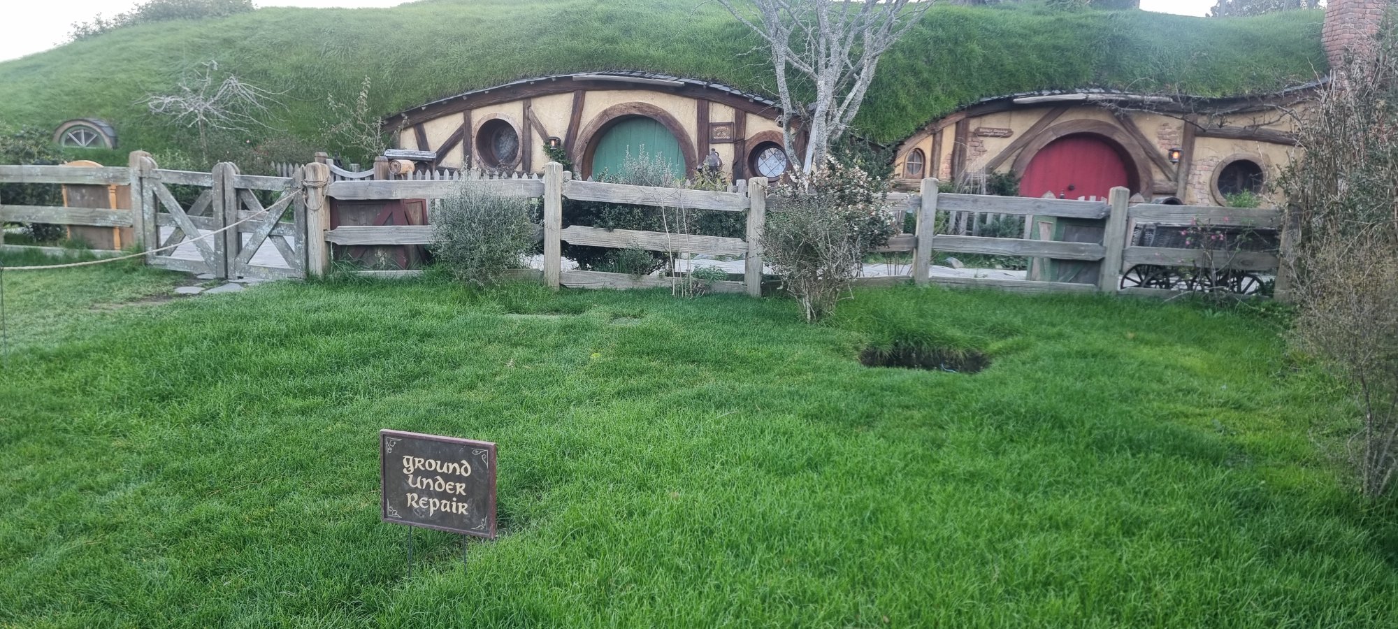 Hobbit holes with round green and red doors set into grassy hillside at Hobbiton Movie Set