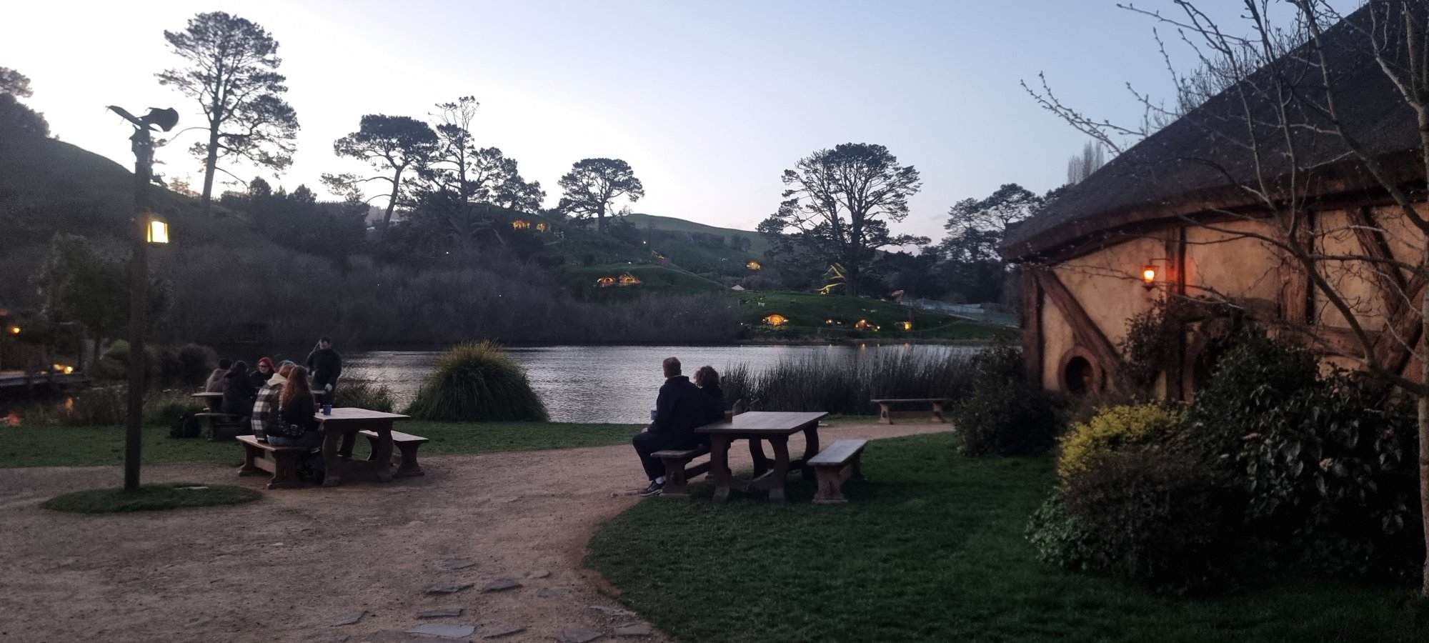 Hobbiton at dusk with the lake, picnic benches and the Green Dragon Inn glowing in evening light