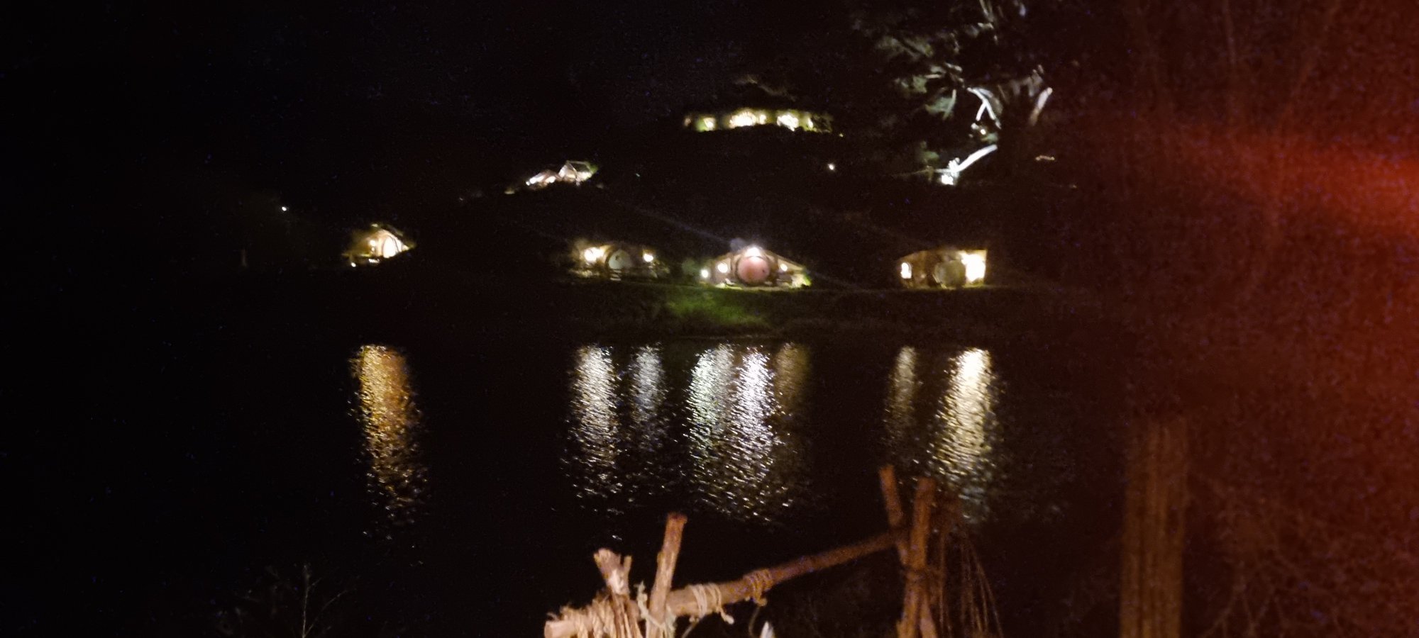 Hobbiton at night with illuminated hobbit holes reflected in the lake