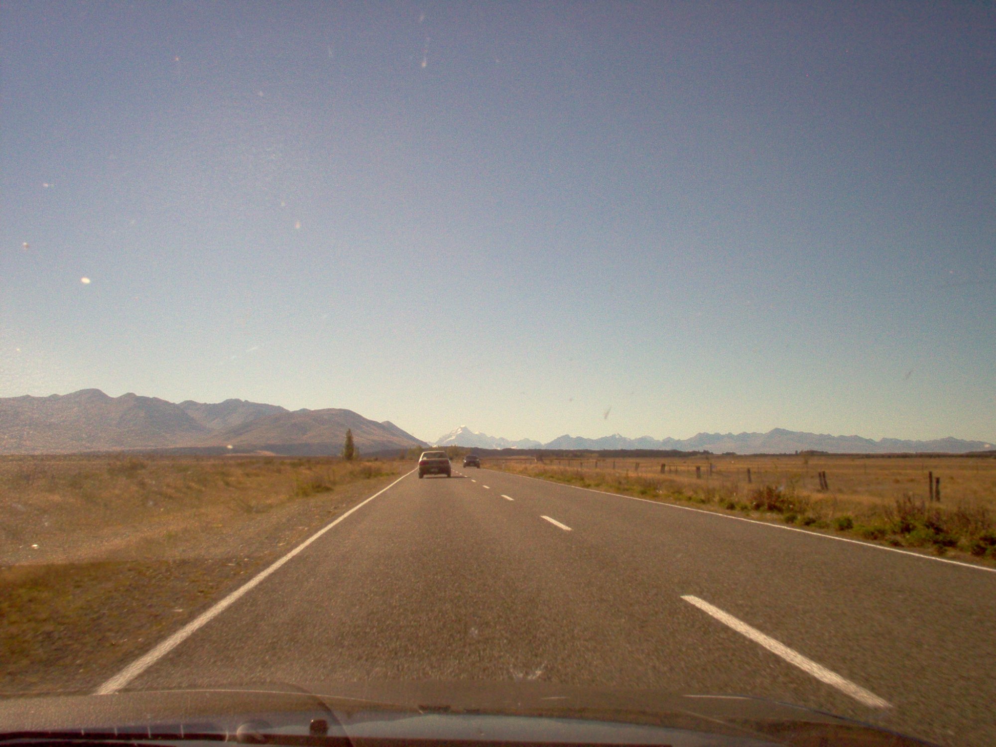 Long straight road through New Zealand countryside with mountains ahead