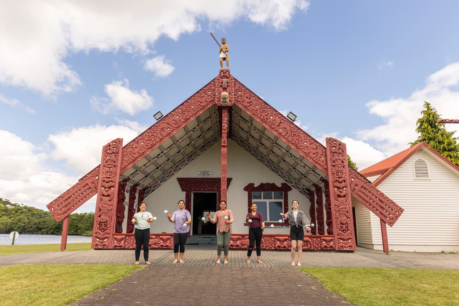 Women performing poi at Te Takinga Marae Rotorua with traditional carved meeting house