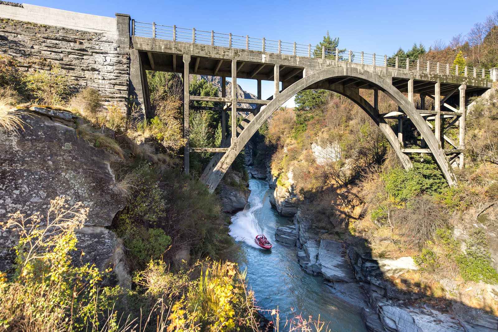 Shotover Jet boat racing through narrow Shotover River canyon under historic bridge Queenstown