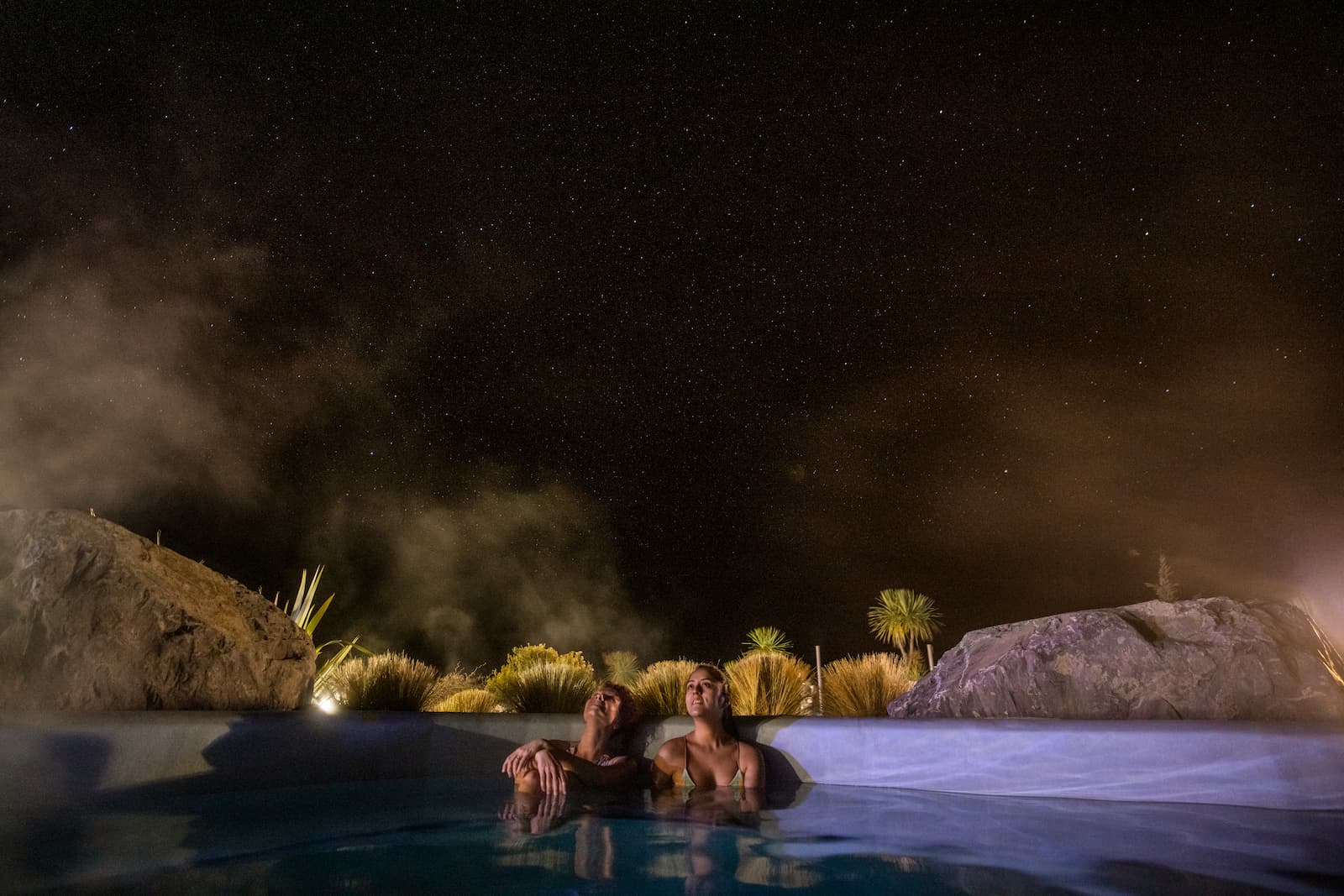 Two people stargazing from hot pools at Tekapo under the Milky Way
