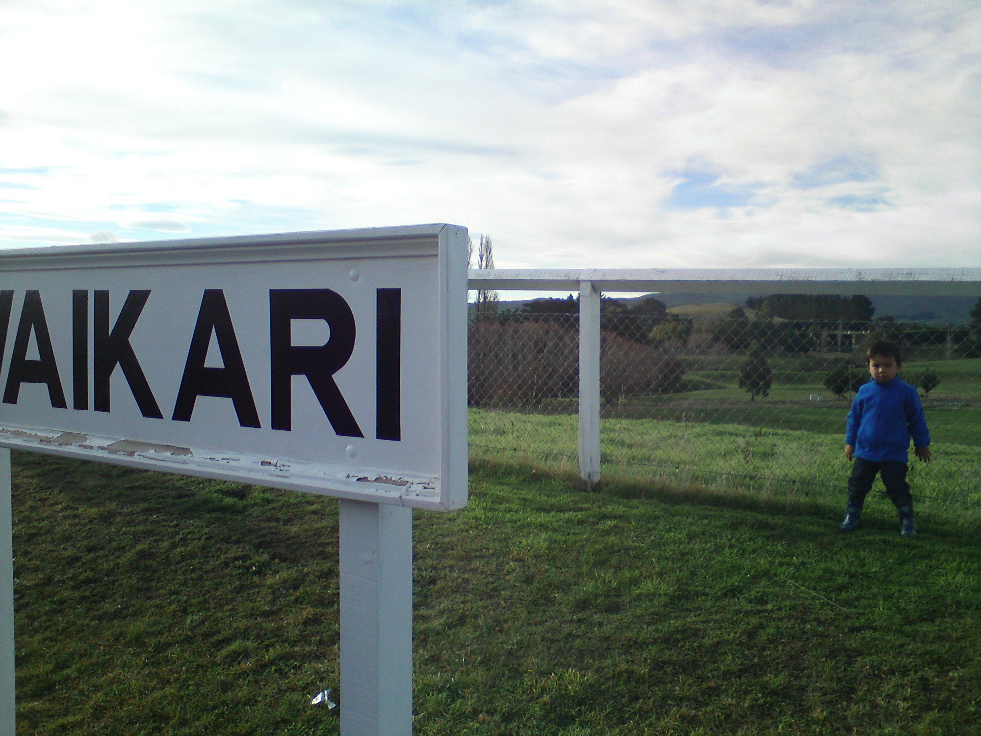 Waikari station sign with green Canterbury farmland and a child in the background